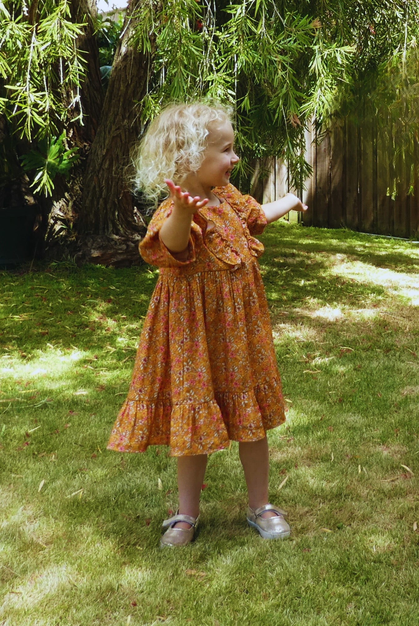 Child in an orange dress standing on grass with trees in the background