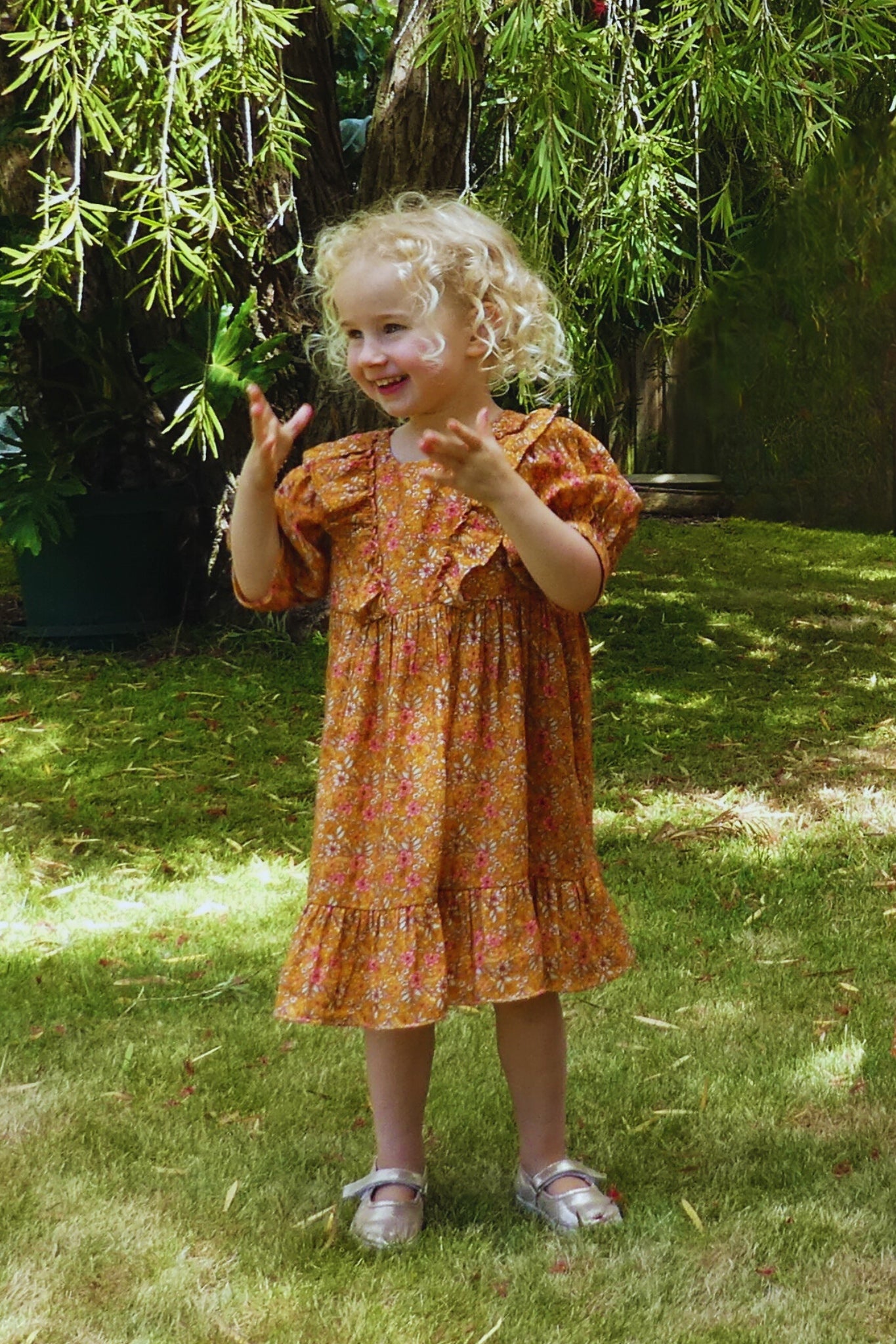 Young girl in a floral dress standing on grass with greenery in the background